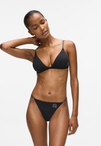 Juodas bikini rinkinys, kuriame yra trikampis liemenėlė su plonomis petnešėlėmis ir atitinkančios kelnaitės. Minkšta medžiaga su minimaliais siuvinėjimais ir išsiuvinėjimo detalėmis.