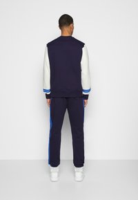 Marinblå och vit träningsoverall med en färgblockerad design, ribbade muddar och blåa sidormen, kompletterad med vita sportskor.