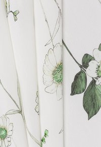 Tissu blanc avec un motif floral comportant des marguerites et des feuilles vertes et beiges, montrant des lignes fines et une surface subtilement texturée.