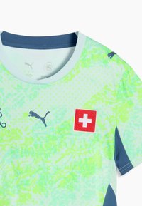 Maillot de sport vert clair et bleu avec col et accents de manches bleu marine, arborant un badge croix suisse rouge et plusieurs logos Puma.