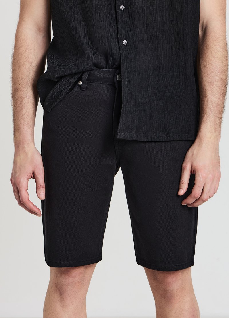 Pantaloni shorts in denim nero con taglio dritto, dotati di chiusura a bottone e cerniera, tasche laterali e una texture sottile nel tessuto.