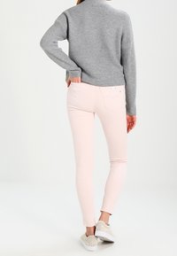 Suéter de punto gris y jeans skinny rosa claro, combinados con zapatos de charol beige, vistos desde atrás. Texturas suaves y diseño ajustado.