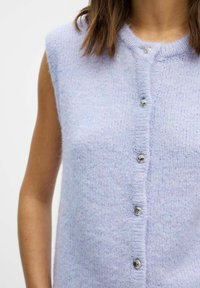 Lyse lilla ærmeløs cardigan lavet af blødt stof, med en knapfront med sølvdetaljer og et tekstureret strikkemønster.