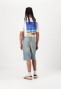 Shorts en denim bleu clair, t-shirt graphique avec un design de coucher de soleil et de palmiers, baskets blanches avec des accents noirs, détails en tissu texturé.