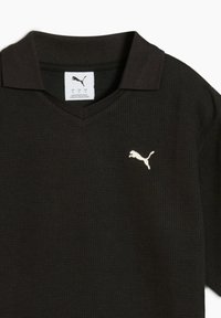 Sort polo skjorte med struktureret stof, v-udskæring og et lille hvidt Puma-logo på venstre bryst. Mærket synligt inden i kraven.