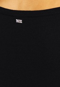 Mustapaita, jossa on pyöreä pääntie, pehmeä kangas ja hopeinen bränditaggi takana. Materiaali on sileä ja hieman teksturoitu.