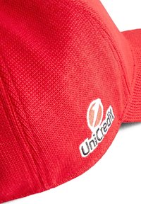 Czerwona czapka baseballowa z teksturowanym materiałem. Posiada białe haftowane logo UniCredit z boku. Daszek jest zaokrąglony.