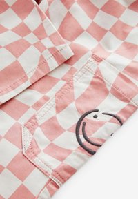 Rosa och vit rutigt tyg med en slät yta, med en sidoficka och en svart broderad smiley-ansikte detaljer.