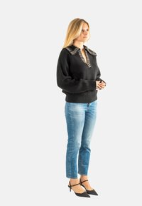 Maglione nero lavorato a maglia con scollo a V profondo e collare borchiato, abbinato a jeans in denim azzurro chiaro e décolleté nere a punta.