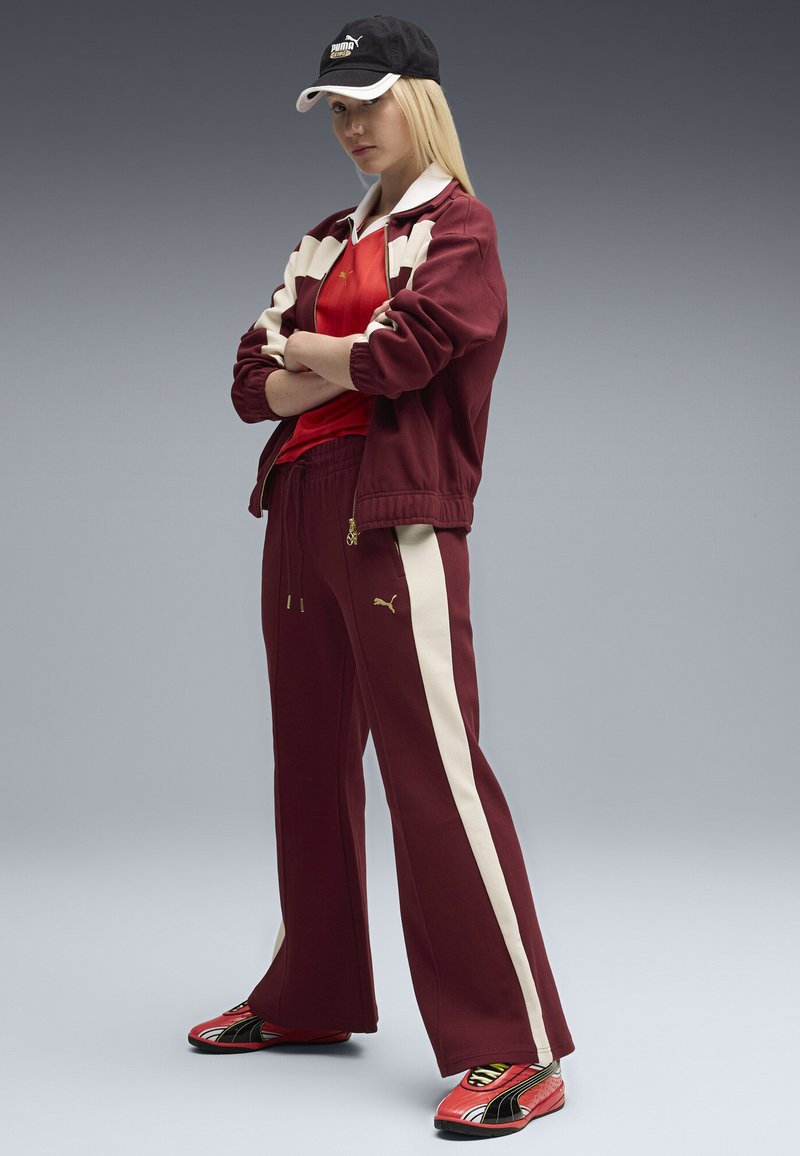 Tuta bordeaux con dettagli crema e un berretto nero. Design sportivo con giacca con zip, pantaloni larghi e sneakers rosse con dettagli gialli.