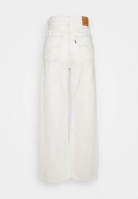 Jeans anchos blancos de mezclilla, con cintura alta, dos bolsillos traseros y costuras claras. Se adjunta una etiqueta de cuero marrón en la cintura.