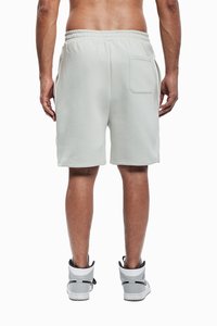 Lys grå treningsshorts laget av myk stoff, med elastisk liv, sidelommer og en baklomme, iført høye sneakers.