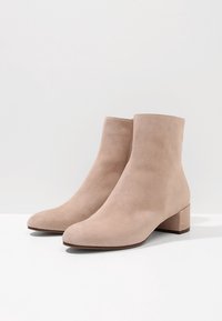 Botas de tobillo de ante beige con punta redondeada y tacón bajo cuadrado. Textura suave con un diseño minimalista.