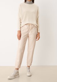 Beige gebreide trui, grijze turtleneck eronder, gecombineerd met lichtbeige broek met een trekkoord in de taille. Lichtgrijze hoge sneakers.