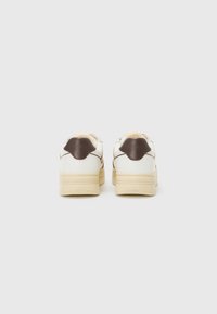 Weiße Sneaker mit einer beigen Sohle, braunen Lederakzenten und einem sternförmigen Rückentab. Die glatte Textur weist ein genähtes Design entlang der Seiten auf.