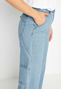 Pantalones de mezclilla color azul claro con corte recto, que presentan un bolsillo lateral y detalles de costura visibles a lo largo de las costuras. Textura suave.