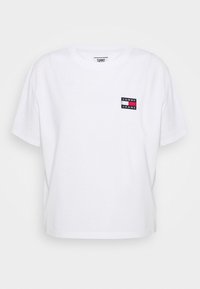 Vitt bomullst-shirt med en kortad design, med en liten svart, röd och blå logotyp på vänster bröst. Kortärmad, rund hals.