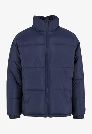 Tums zilā krāsā pūkains apģērbs ar augstu apkakli, priekšējais rāvējslēdzis un horizontāli quiltēti posmi. Izgatavots no gludas, vieglas auduma.