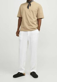 Beżowa bawełniana koszulka, luźny fason, zestawiona z białymi lnianymi spodniami i czarnymi klapkami. Dodatki to czarny wzorzysty szalik związany na szyi.