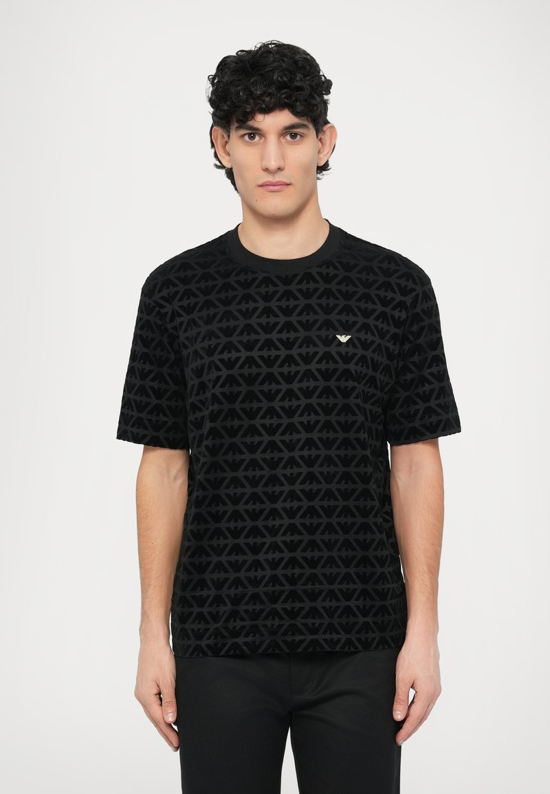 Čierne tričko s krátkym rukávom so štruktúrovaným vzorom preplietaných trojuholníkov, okrúhlym výstrihom a malým zlatým emblémom na hrudi.