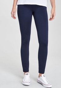 Marineblauwe leggings van een gladde, rekbare stof met een aansluitend ontwerp, gecombineerd met witte lage sneakers. Geen zichtbare details of patronen.
