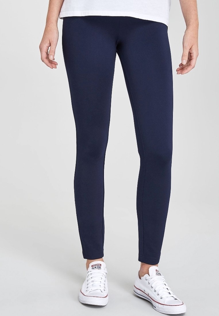 Marineblauwe leggings van een gladde, rekbare stof met een aansluitend ontwerp, gecombineerd met witte lage sneakers. Geen zichtbare details of patronen.