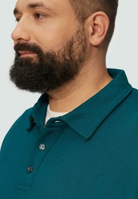 Türaqua Polo-Shirt mit strukturiertem Kragen, ausgestattet mit einer Drei-Knopf-Leiste und strukturiertem Stoff. Nahaufnahme im Profil.
