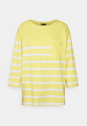T-shirt listrada em amarelo e branco com decote redondo, mangas três quartos e um bolso no lado esquerdo do peito. Tecido macio e leve.