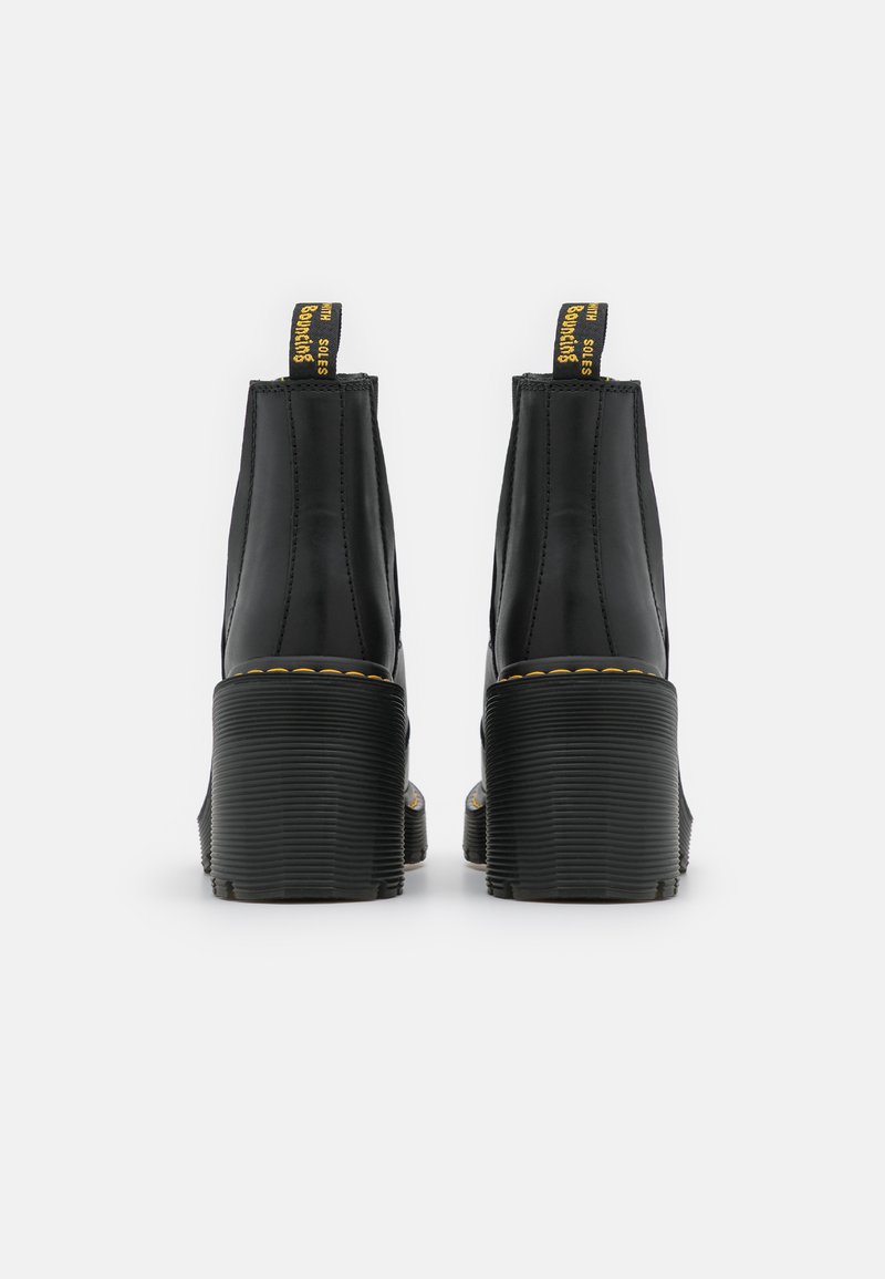 Bottes chelsea noires avec une finition lisse, semelle en caoutchouc texturée, coutures jaunes et une languette avec un logo audacieux à l'arrière.