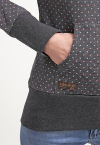Sudadera gris oscura con lunares rosas y grises, que cuenta con un bolsillo frontal y un dobladillo etiquetado en cuero con la marca "RAGWEAR".