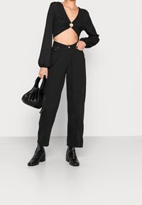 Schwarzes Crop-Top mit einer verdrehten Vorderseite und kreisförmigem Ausschnitt, kombiniert mit hochgeschnittenen schwarzen weit geschnittenen Hosen und schwarzen Absatzstiefeletten.
