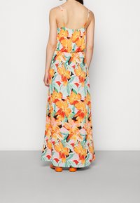 Maxi-jurk met een helder oranje en roze bloemenprint op een lichtblauwe achtergrond. Heeft dunne banden, een relaxte pasvorm en een vloeiende stijl.