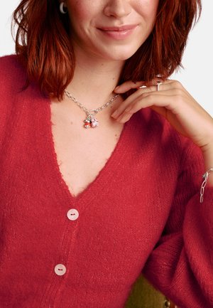 Roter strukturierter Cardigan mit V-Ausschnitt und drei Knöpfen. Dicke silberne Ketten Halskette mit Charms, getragen auf einem hellen Hautton.