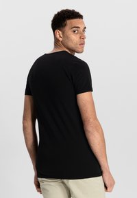 Black short-sleeve t-shirt with a round neckline, featuring a fitted design and smooth texture. Worn with light-colored pants.