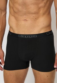 Boxeri negri dintr-un material neted, cu un design ajustat; prezintă un brâu elastic cu logo-ul "Kappa" în gri contrastant.