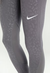 Leggings sportivi grigi con un motivo testurizzato, tessuto liscio e logo Nike bianco sulla coscia. Progettati per comfort e flessibilità.