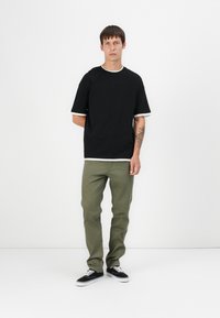 Black short-sleeve t-shirt with white cuffs, paired with green pants and black sneakers. Simple, casual design with a relaxed fit.