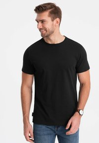 Sort crew-neck T-shirt i en glat bomuldsblanding med korte ærmer og lige snit. Bærer den med blå jeans og et ur.