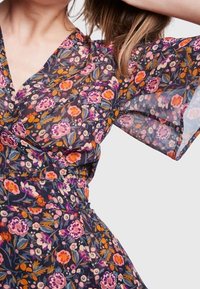 Blumenkleid mit einem dunklen Hintergrund und bunten Blumen in Rosa, Orange und Lila. Durchsichtige, ausgestelltÄrmel und taillierte Passform.