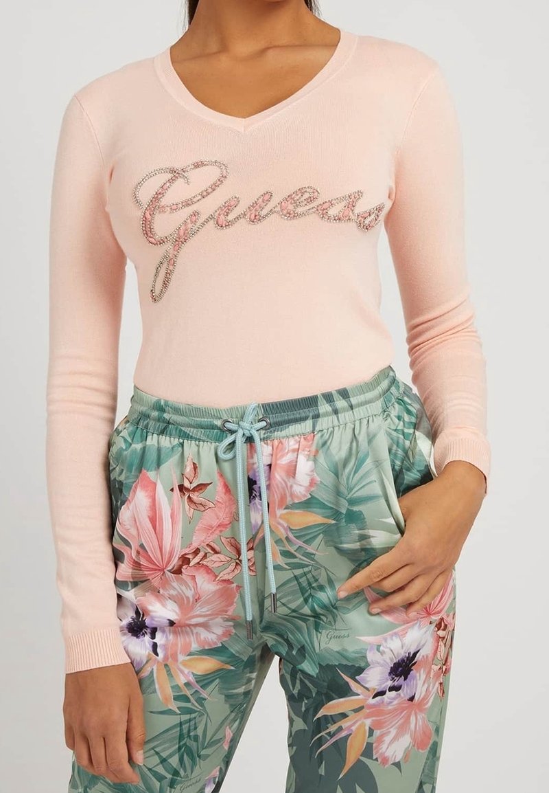 Top rosa claro de manga larga con "Guess" en adornos brillantes, combinado con pantalones jogger verdes con estampado floral y cintura con cordón.
