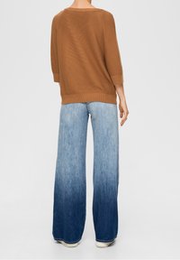 Brun ribbad tröja med trekvartslånga ärmar, kombinerad med bredbenade jeans i ljus till mörk gradient, med ett mjukt material och avslappnad passform.