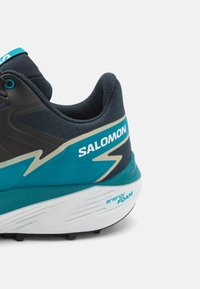 Scarpa da corsa con tomaia in mesh blu scuro, dettagli turchesi e suola bianca dotata di schiuma energetica. Logo "SALOMON" in evidenza.