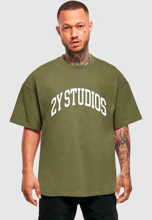 Olivengrünes, oversized T-Shirt mit kurzen Ärmeln, auf dem "2Y STUDIOS" in fettem weißen Bogen-Text über der Brust steht. Aus Baumwollstoff.