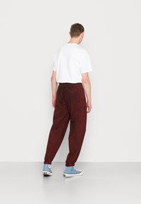 Calças largas bordeaux com um cós elástico e punhos, combinadas com uma t-shirt branca lisa e ténis de cano alto azul claro.