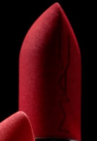 Un rouge à lèvres rouge sous forme de bâton, avec une finition mate, un embout pointu et un détail de logo gravé, sur fond noir.