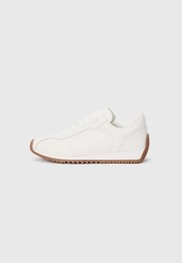 White sneaker with smooth leather upper, textured rubber sole, rounded toe, and subtle stitching details. Contrasting brown rubber outsole.