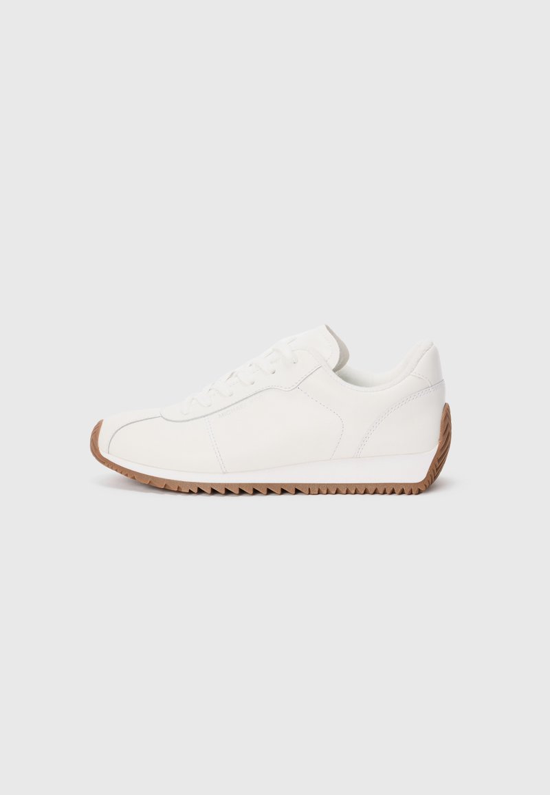 White sneaker with smooth leather upper, textured rubber sole, rounded toe, and subtle stitching details. Contrasting brown rubber outsole.