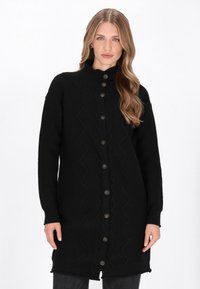 Czarny długi kardigan z wysokim kołnierzem, zapięciem na guziki z przodu, wzorem w zygzaki na tkaninie oraz prążkowanymi mankietami i dołem. Wykonany z teksturowanego materiału.