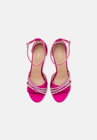 Sandali con tacco alto in satin rosa, con cinturino alla caviglia, caratterizzati da un design incrociato e dettagli in strass sulle cinghie.