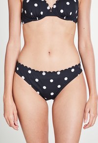 Ensemble de bikini noir à pois blancs. Le soutien-gorge présente des bords festonnés ; le bas a un design et une coupe similaires, mettant en valeur le motif.